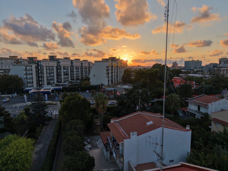 Tramonto sui palazzi di Bari visto dall'alto, con i tetti e le antenne in controluce.